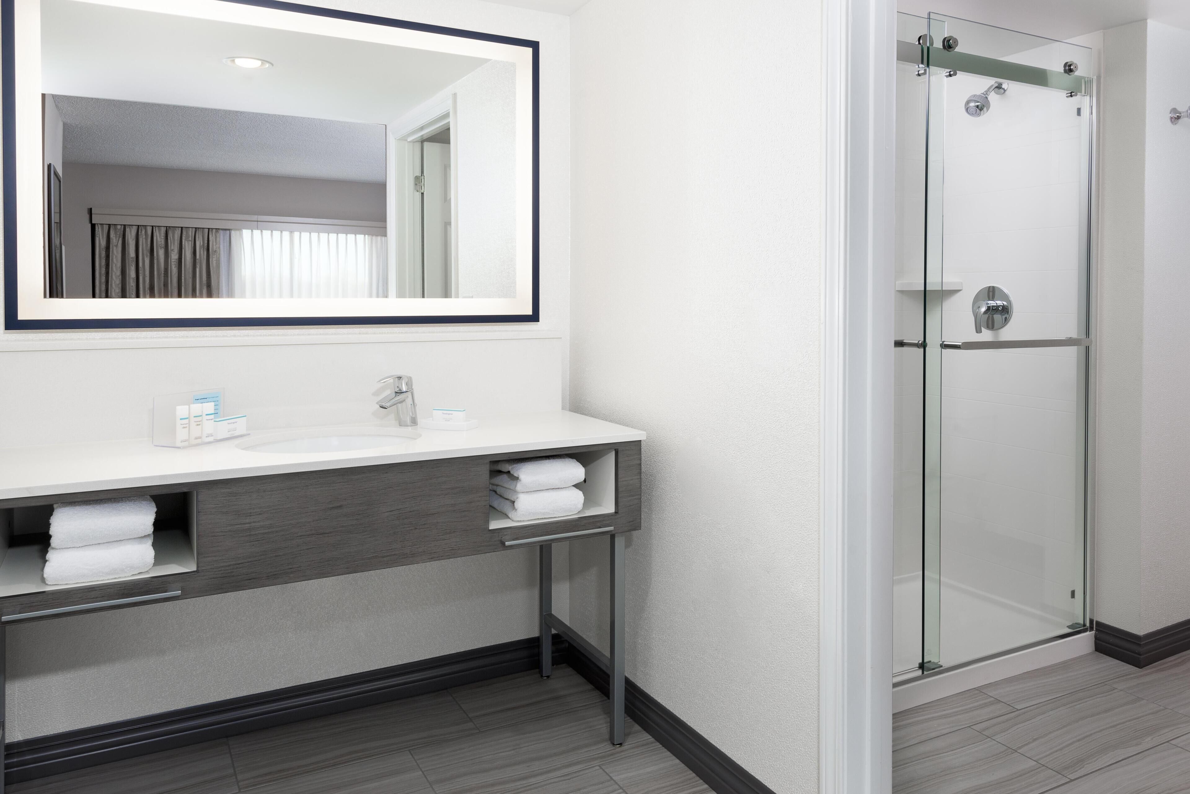 A modern bathroom with a large mirror, two sinks, a glass shower enclosure, and a towel rack.