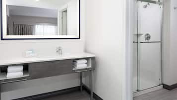 A modern bathroom with a large mirror, two sinks, a glass shower enclosure, and a towel rack.