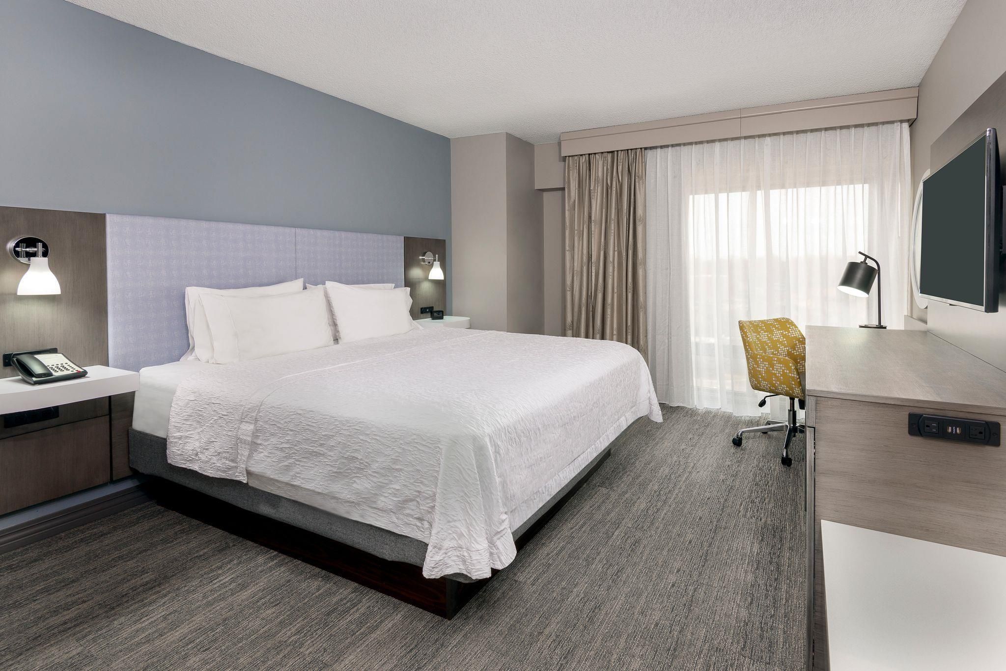 Une chambre d’hôtel comprenant un lit, des tables de chevet, un bureau avec une chaise, une télévision et des rideaux.