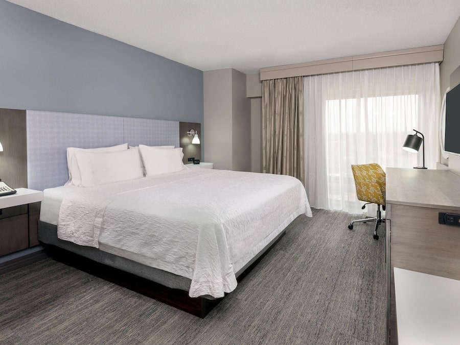 Une chambre d’hôtel comprenant un lit, des tables de chevet, un bureau avec une chaise, une télévision et des rideaux.
