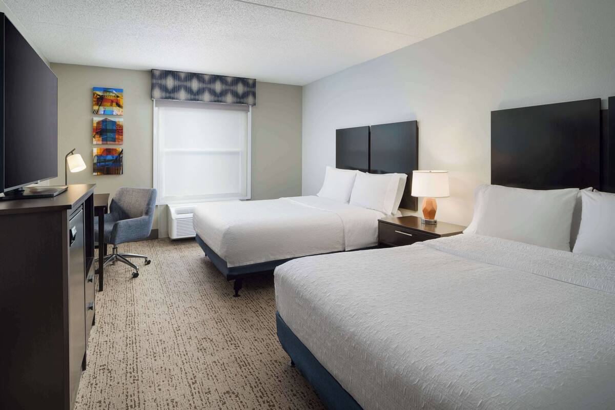 A hotel room with two beds, a desk with a computer, a chair, and a TV.