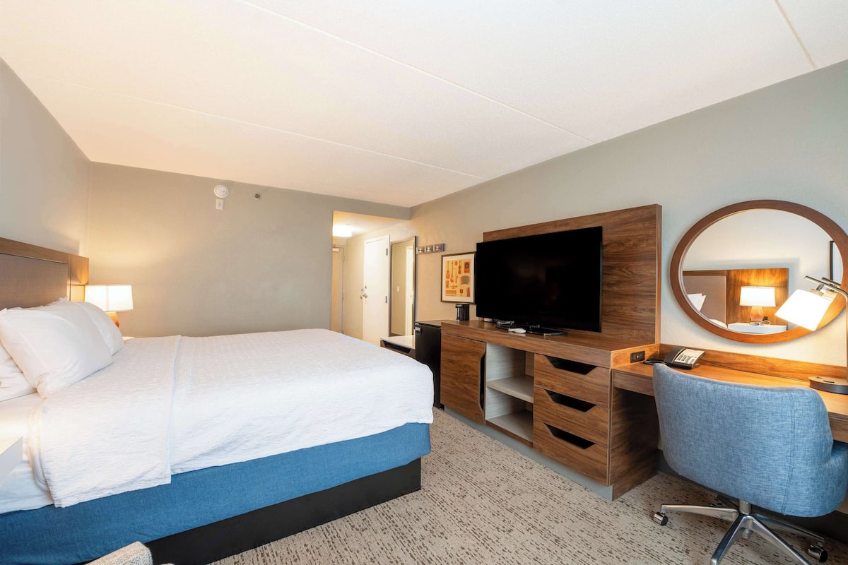 A hotel room with a bed, a desk, a television, a mirror, and a lamp.