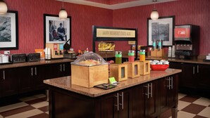 A breakfast bar with a sign that reads "HAPPY BREAKFAST STARTS HERE," a juice dispenser, and various food containers. - Hampton Inn Niagara Falls (Niagara Falls)
