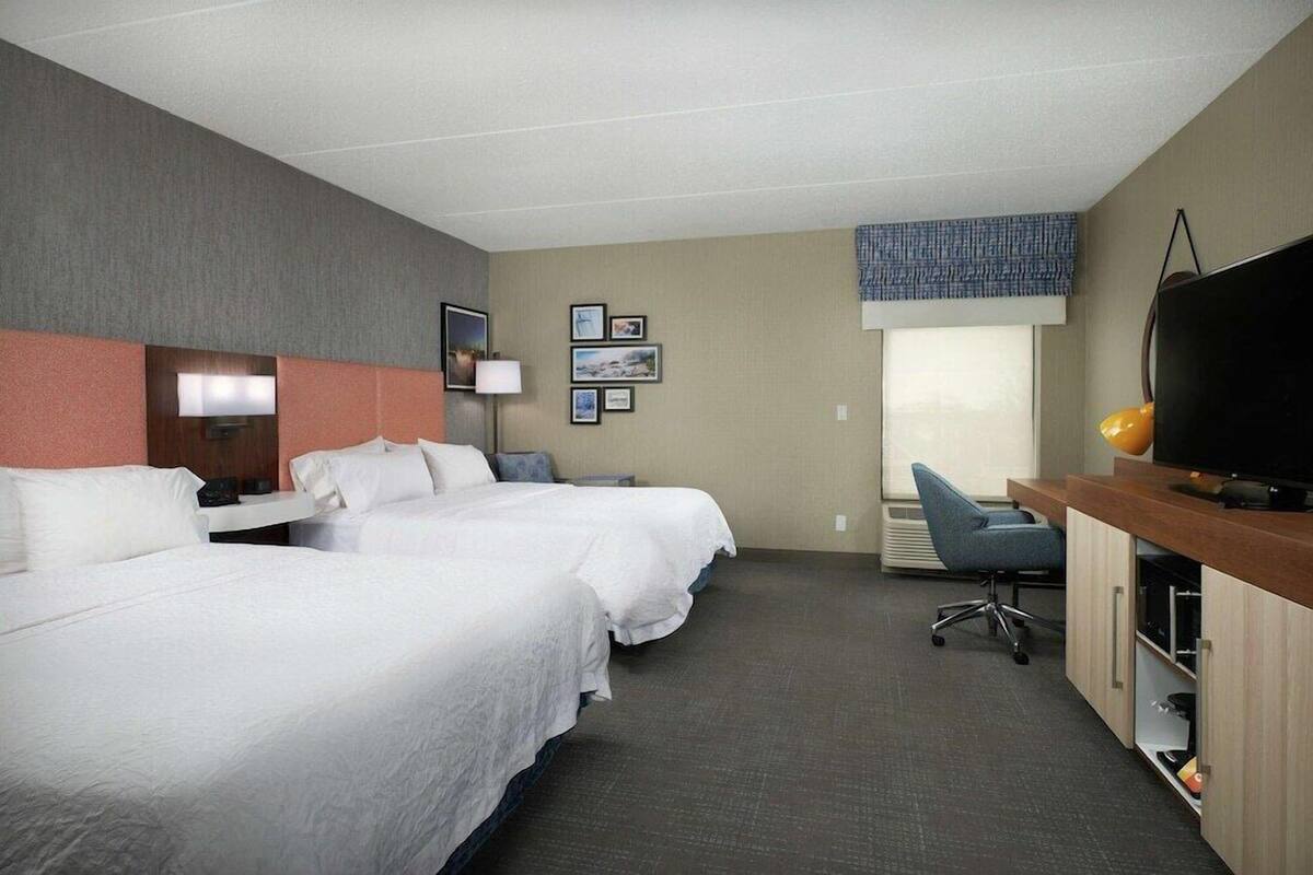 A hotel room with two beds, a desk, a television, and a window.