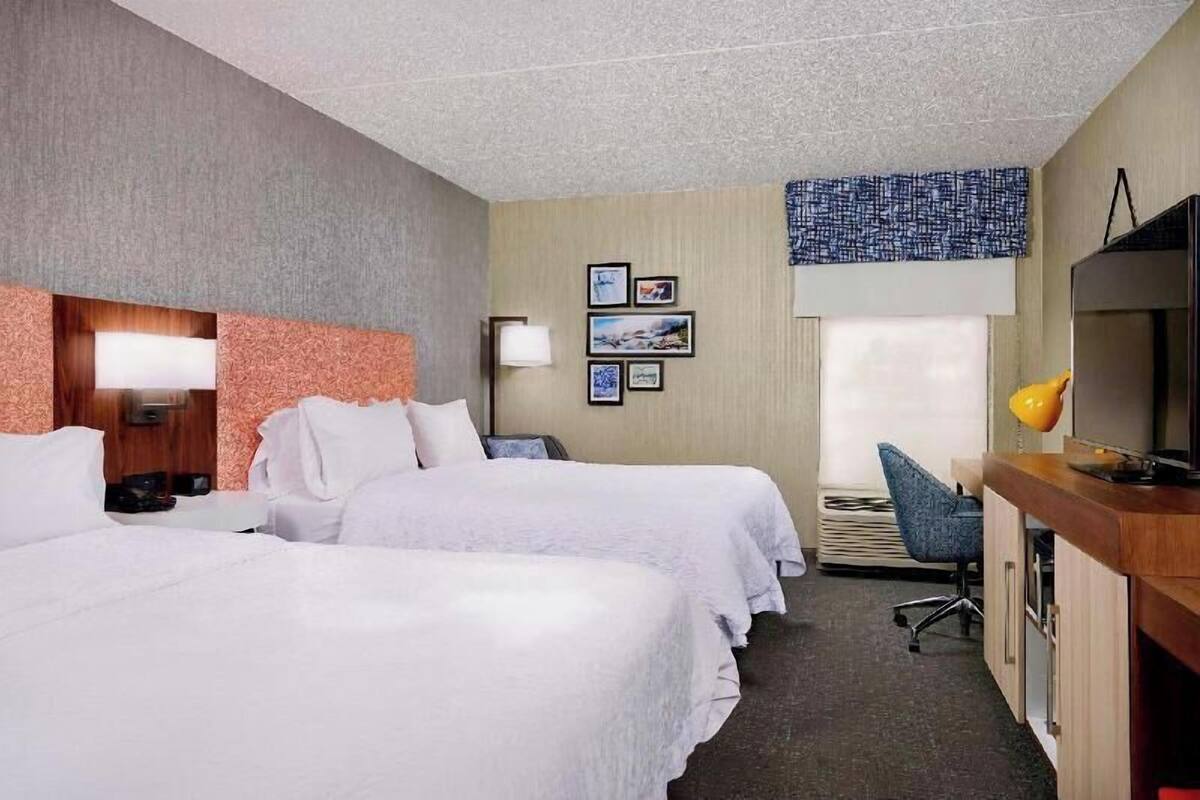 Une chambre d’hôtel avec deux lits, un bureau, une chaise, une télévision et des tableaux encadrés au mur.