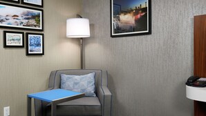 A hotel room with a gray sofa, a small table, a lamp, and framed pictures on the wall. - Hampton Inn Niagara Falls (Niagara Falls)