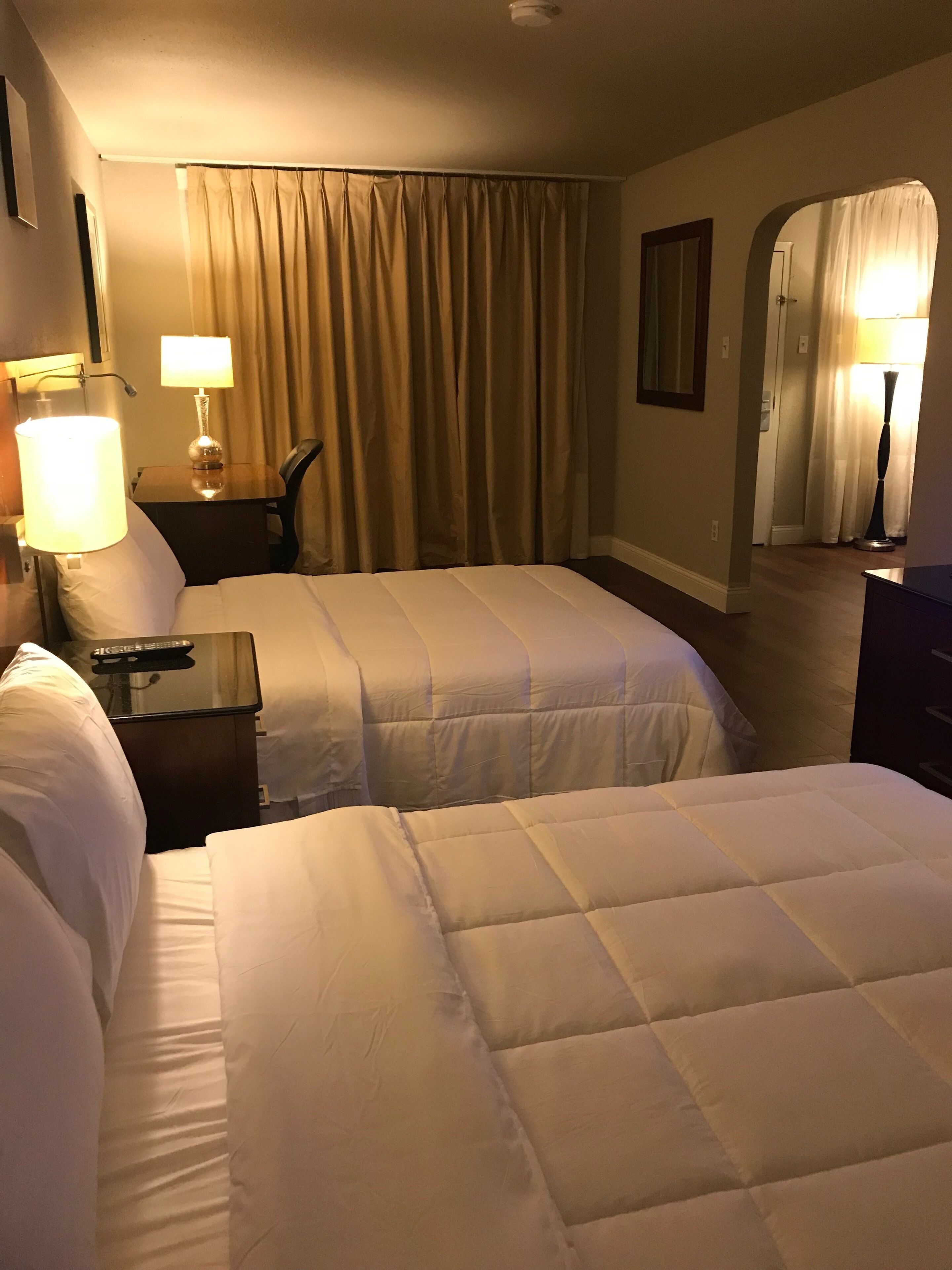 A hotel room with two beds, a desk, a chair, and a lamp.