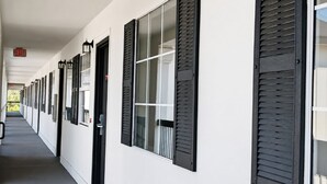 Un pasillo de hotel con persianas negras en las ventanas, fachada blanca y señal de salida.