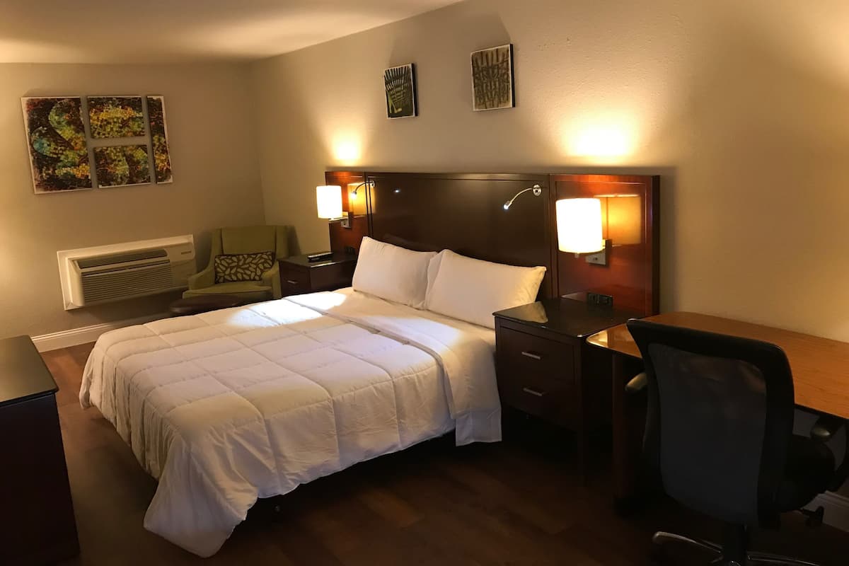 A hotel room with a large bed, two bedside tables, a desk with a chair, and two wall-mounted lamps.