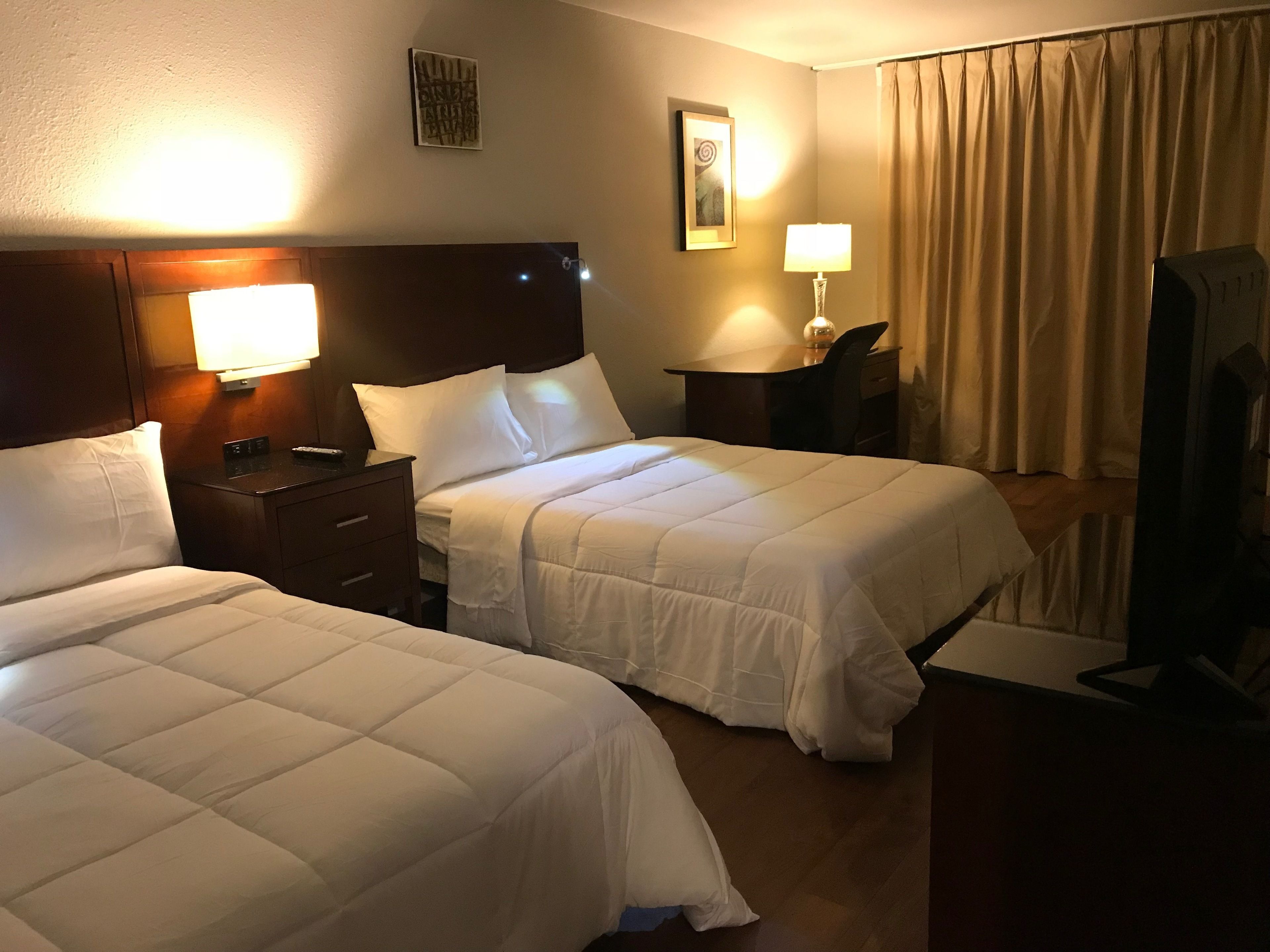 Une chambre d’hôtel avec deux lits, un bureau, une chaise, une lampe et un tableau au mur.