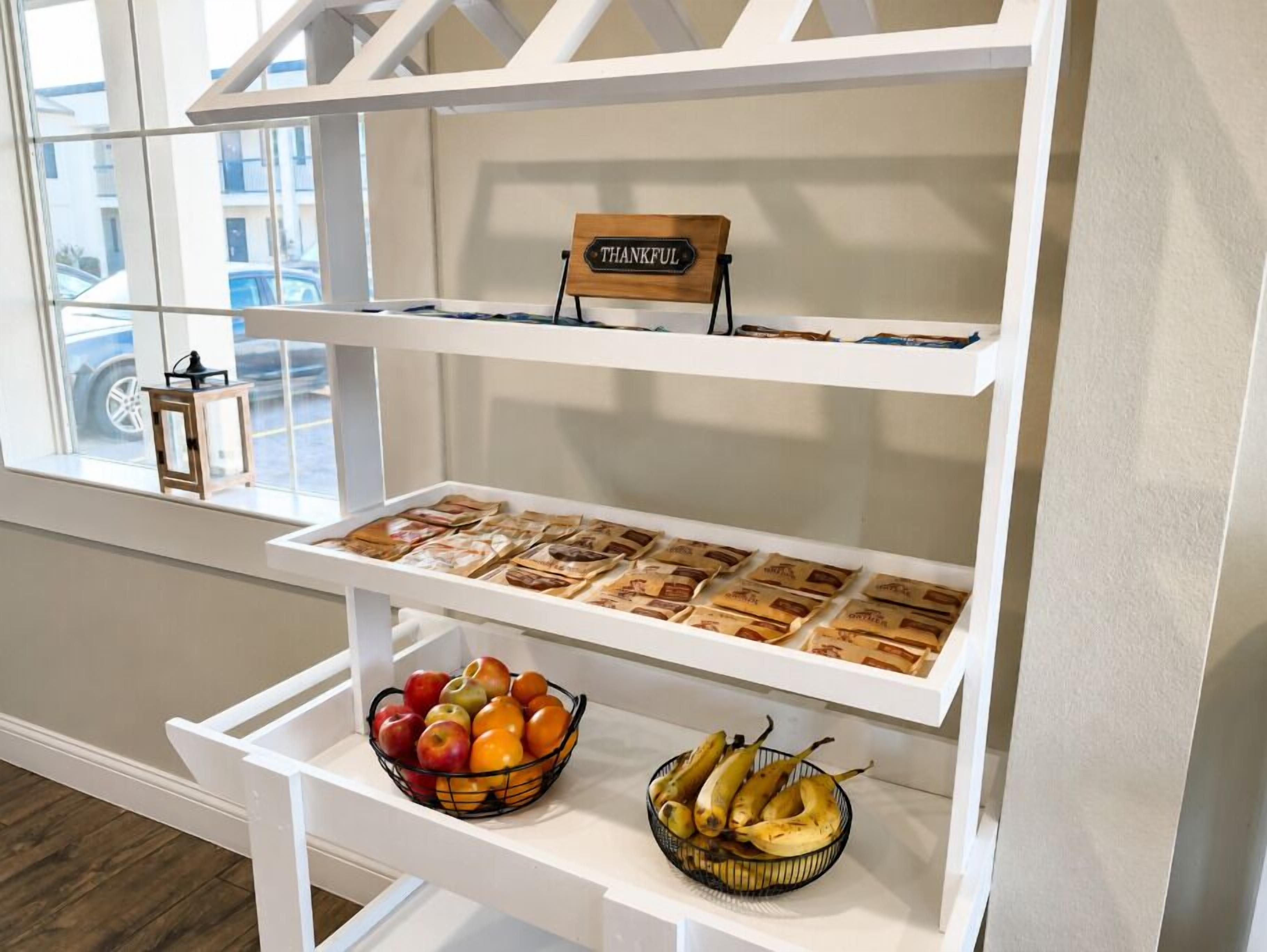 A breakfast buffet setup with a sign reading 'THANKFUL,' a variety of packaged foods, and fresh fruit on the lower shelf.