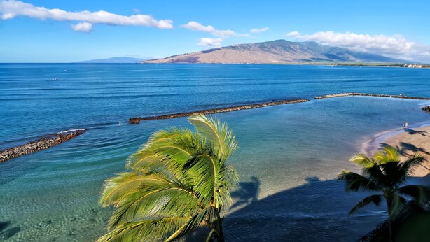 A coastal view with clear water, a rocky breakwater, and a distant mountain range.