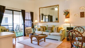 A living room with a sofa, a coffee table, wicker chairs, a TV, and a large mirror.