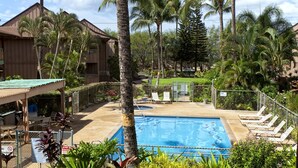 A pool area with lounge chairs, a wooden building, and palm trees.