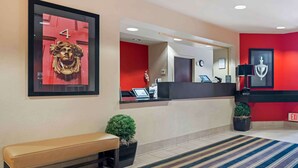 A hotel reception area with a red wall, a reception desk, a bench, and a framed artwork.