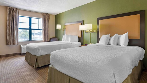 A hotel room with two beds, a large window, and a view of the outdoors.