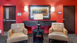 A lobby with two leather armchairs, a black side table, a welcome sign, and two wall-mounted lamps.