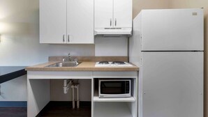 A compact kitchenette with white cabinets, a sink, a microwave, and a stove.