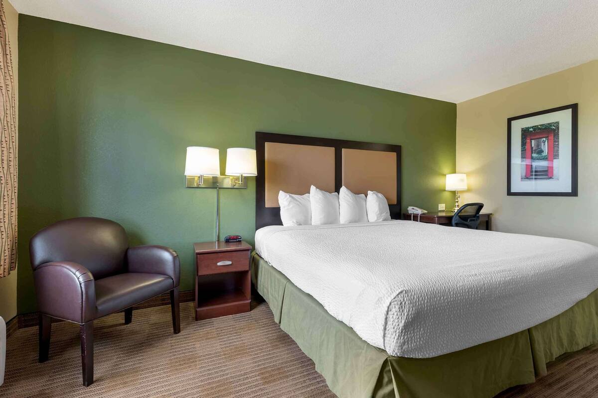 Een hotelkamer met een groot bed, een stoel, een nachtkastje en een lamp.