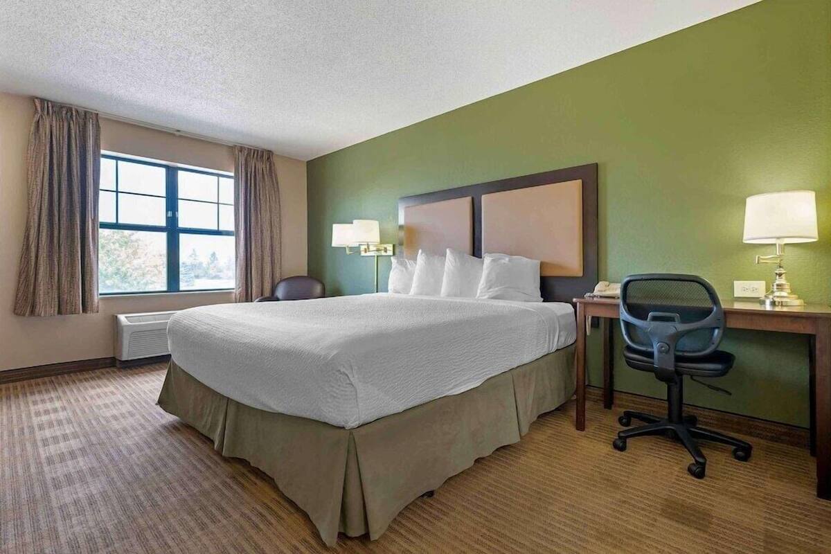 Een hotelkamer met een groot bed, een bureau met stoel, een lamp en een raam met gordijnen.