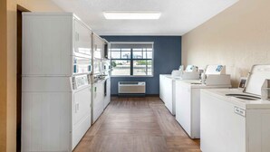A laundry room with white appliances, a window with a view, and a wooden floor.