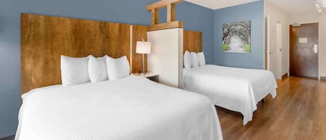 Une chambre d’hôtel avec deux lits, une tête de lit en bois, une table de chevet avec une lampe et un tableau au mur.