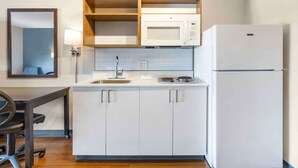 A compact kitchen with white cabinets, a microwave, a refrigerator, and a sink.