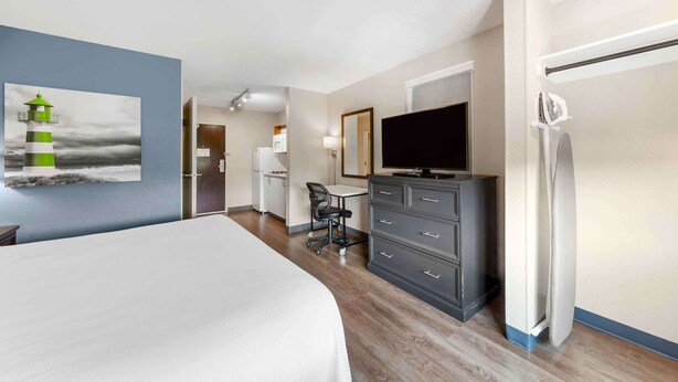A hotel room with a bed, a desk, a chair, a TV, a dresser, and a refrigerator.