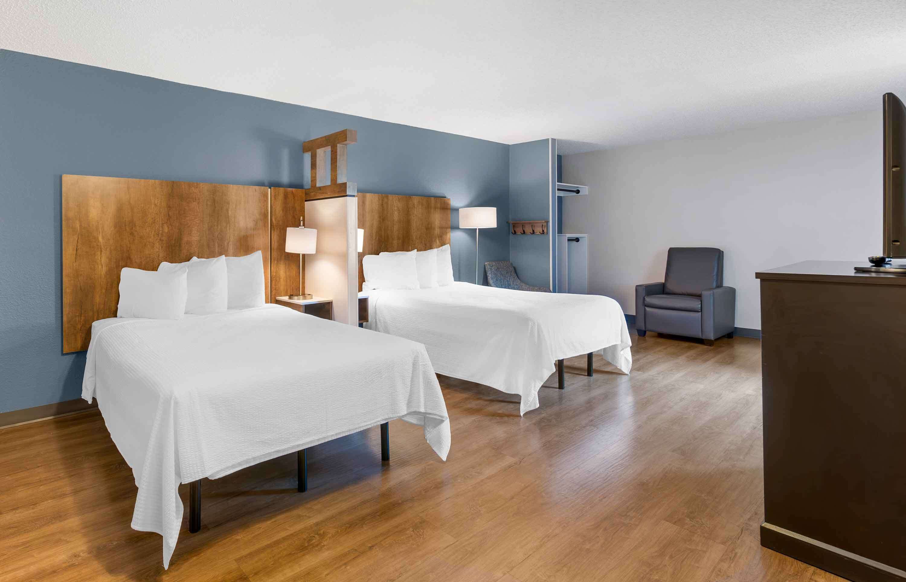 A hotel room with two beds, a desk, a chair, and a TV.