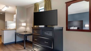 A modern hotel room with a flat-screen TV, a desk with drawers, a mirror, and a kitchenette with a refrigerator. - Extended Stay America Suites Fort Worth City View (Fort Worth)