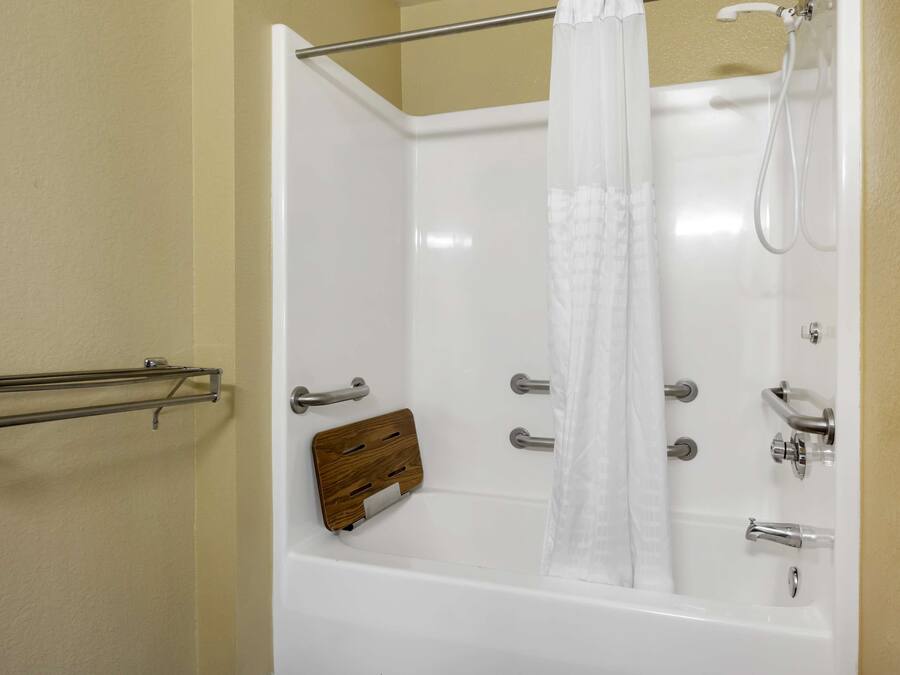 Une baignoire blanche avec un pommeau de douche, un porte-savon en bois et un porte-serviettes en métal.