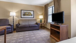 Habitación de hotel con sofá, dos lámparas, televisor de pantalla plana y un cuadro en la pared.