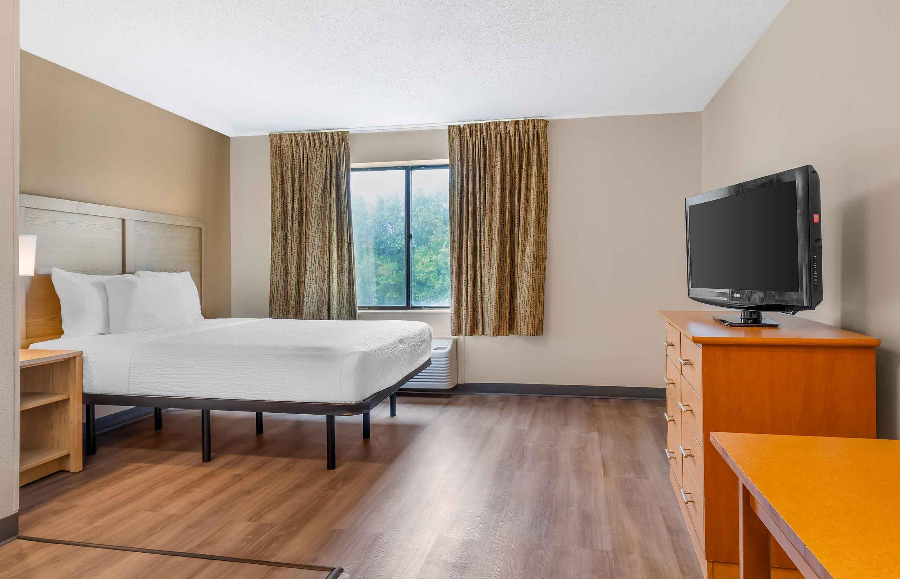 Une chambre d’hôtel avec un lit, un téléviseur posé sur une commode en bois et une fenêtre avec des rideaux.