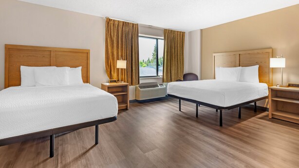 A hotel room with two beds, wooden headboards, a window with curtains, a desk, a chair, and an air conditioning unit. - Extended Stay America Suites Fort Worth Fossil Creek (Fort Worth)