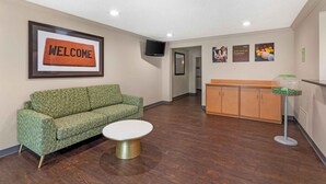 A reception area with a green sofa, a white coffee table, a welcome mat, a TV, and a grab-and-go breakfast sign. - Extended Stay America Suites Fort Worth Fossil Creek (Fort Worth)
