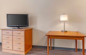 Een kamer met een houten dressoir met lades, een televisie erop en een tafel met een lamp.