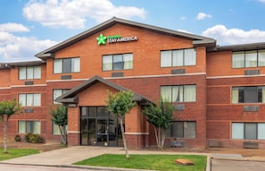 Een gebouw van baksteen met een groen logo en een bord met de tekst 'Extended Stay America', meerdere ramen en een zichtbare ingang.