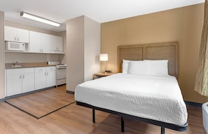 Een hotelkamer met een bed, nachtkastje, lamp, magnetron en kitchenette.