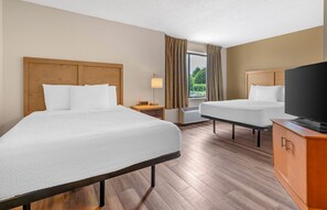 Een hotelkamer met twee bedden, een televisie, een nachtkastje en een raam met gordijnen.