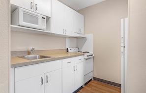 A kitchen with white cabinets, a microwave, a stove, and a refrigerator. - Extended Stay America Suites Fort Worth Fossil Creek (Fort Worth)