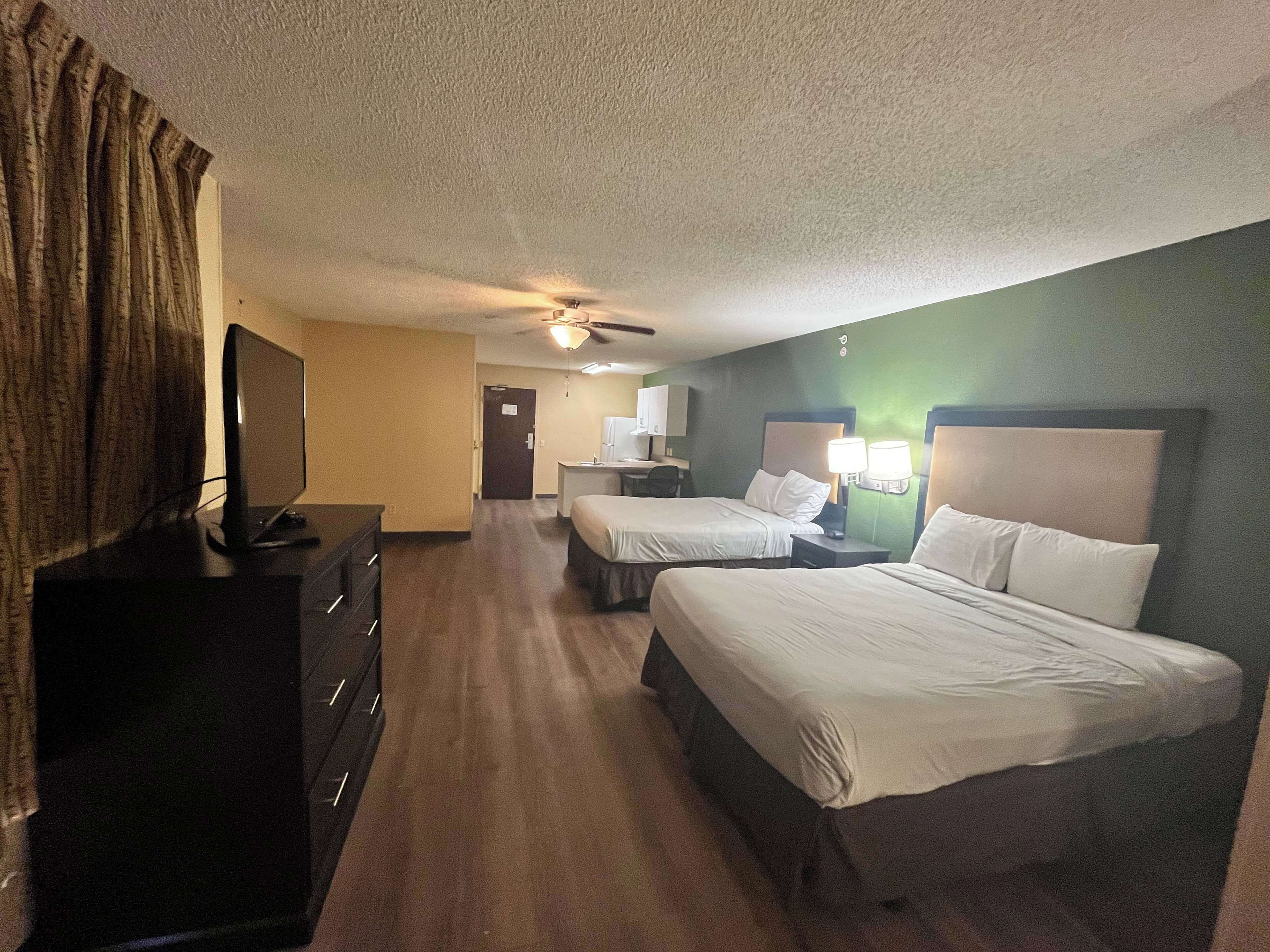 A hotel room with two beds, a TV, a desk, and a ceiling fan.
