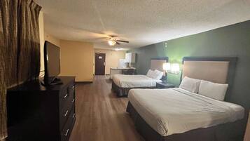 A hotel room with two beds, a TV, a desk, and a ceiling fan.