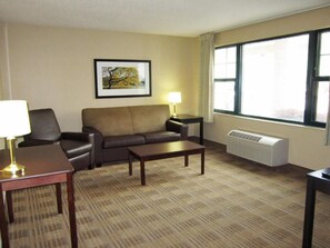 A hotel room with a sofa, a coffee table, a lamp, a picture on the wall, and a large window. - Studio 6 Memphis, TN – East Memphis (Memphis)