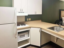 A compact kitchen with white cabinets, a built-in microwave, a stove, and a sink.