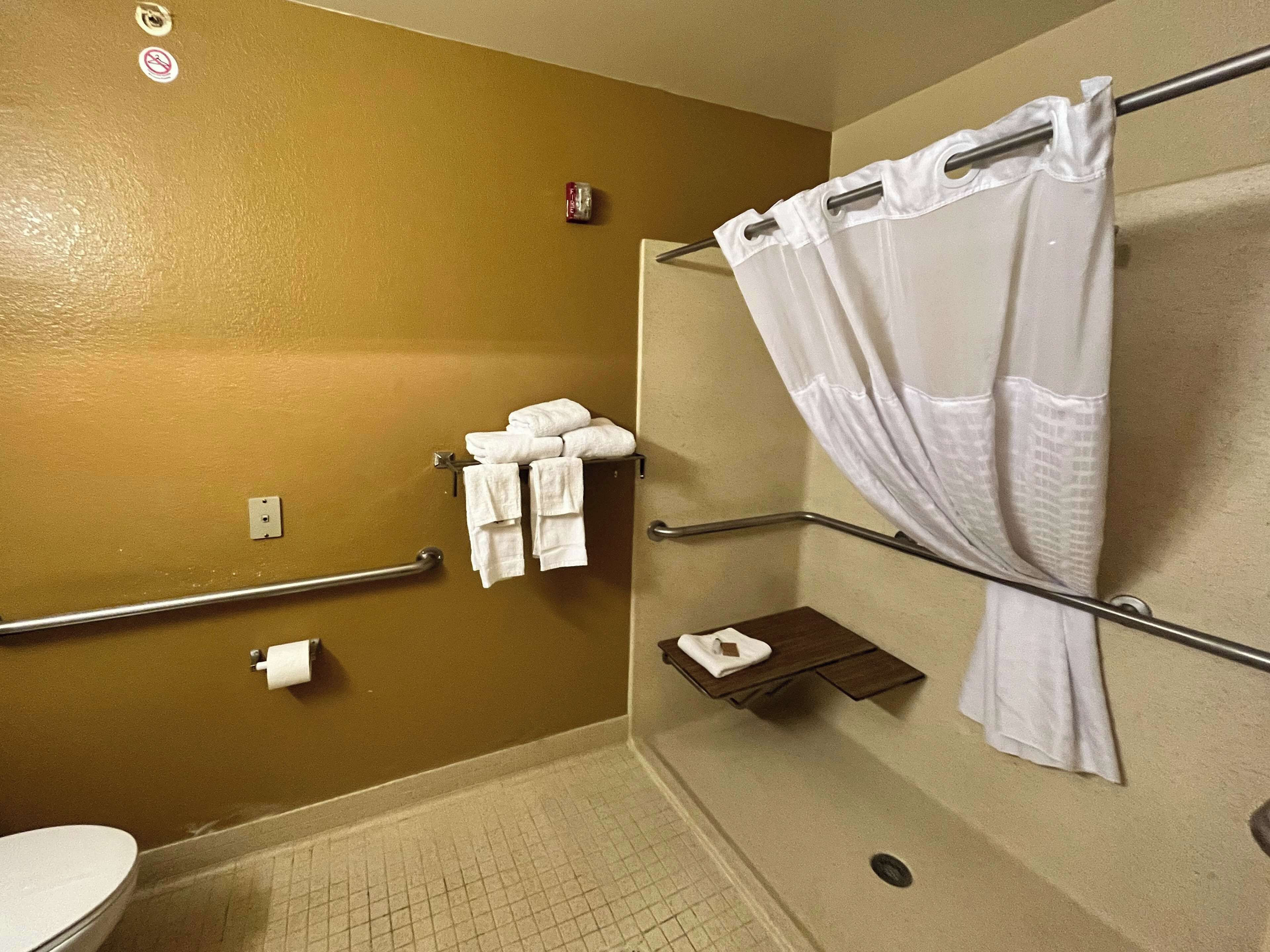 A bathroom with a toilet, a shower with a white curtain, and a towel rack with folded towels.