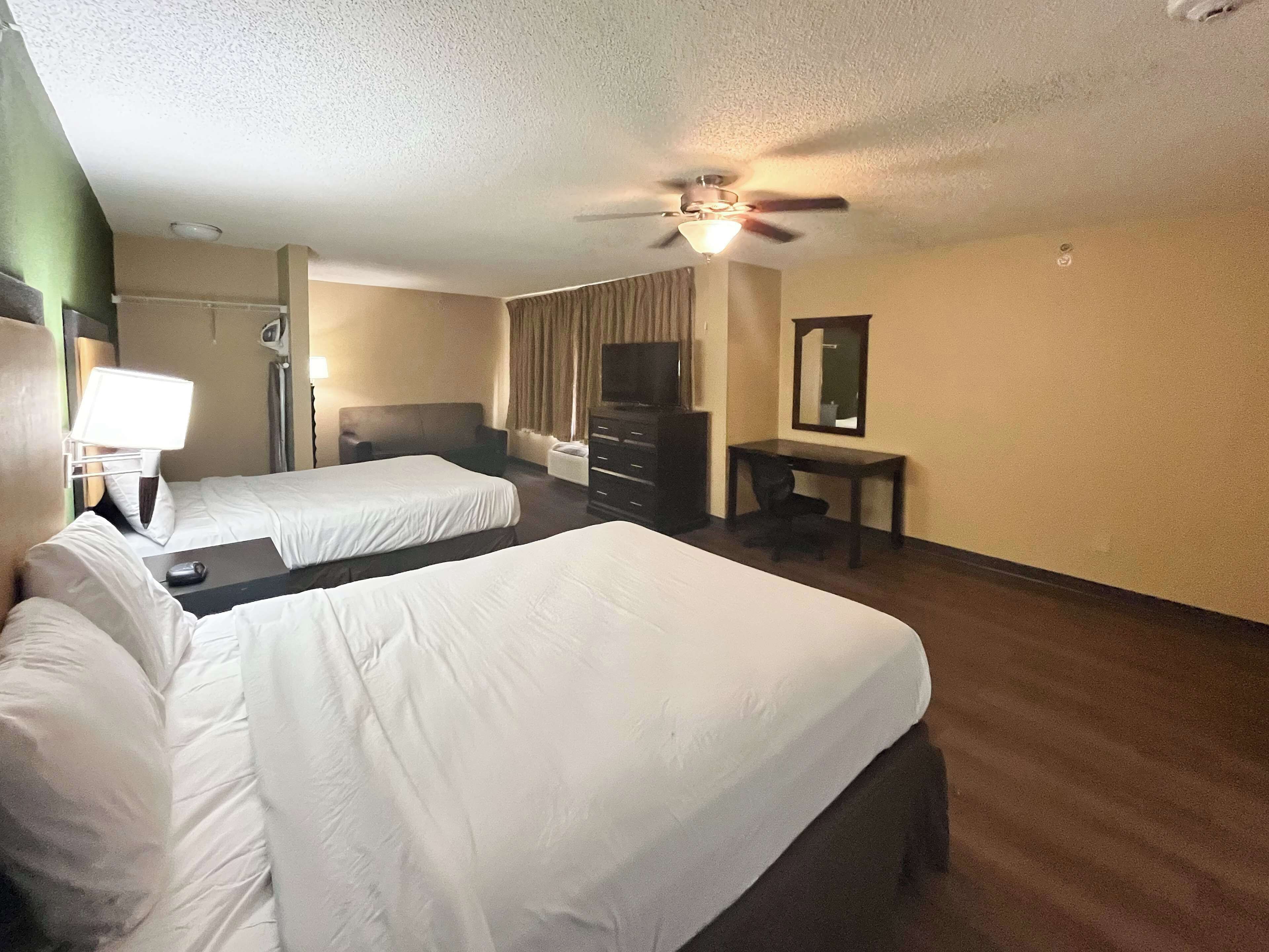 A hotel room with two beds, a desk, a chair, a TV, and a ceiling fan.