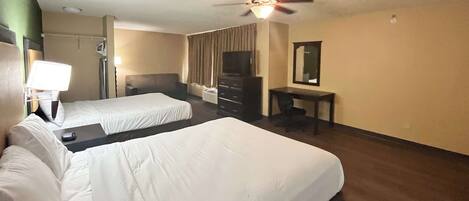 A hotel room with two beds, a desk, a chair, a TV, and a ceiling fan.