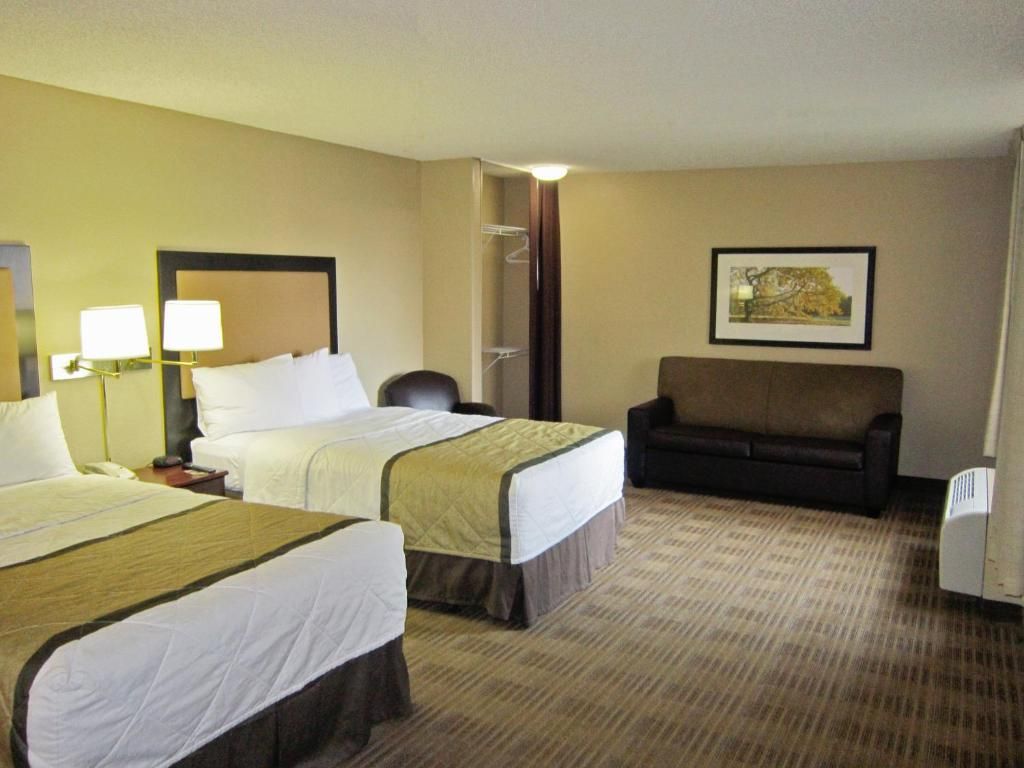 A hotel room with two beds, a sofa, a chair, a desk, and a framed picture on the wall.