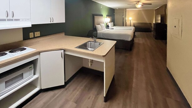 Une chambre d’hôtel compacte comprenant un coin cuisine, un lit, une table de chevet et un ventilateur de plafond.
