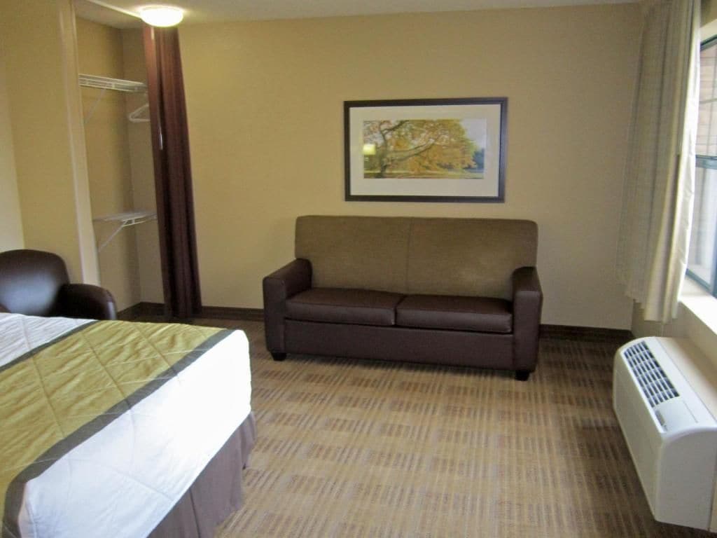 A hotel room with a bed, a sofa, a framed picture on the wall, and a window.